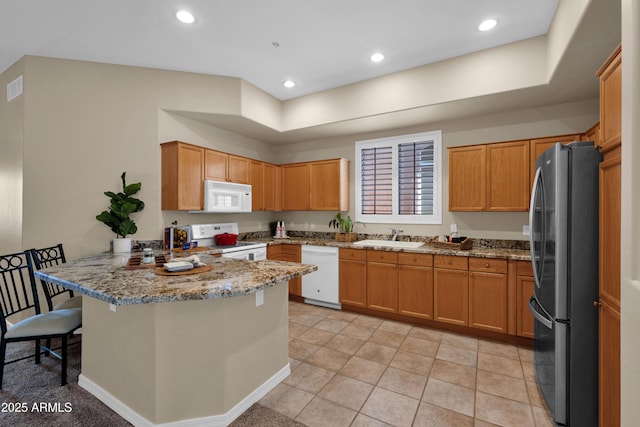 kitchen with light stone counters, a sink, white appliances, a peninsula, and visible vents