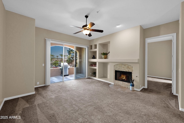 unfurnished living room featuring a tiled fireplace, carpet floors, built in features, and a ceiling fan