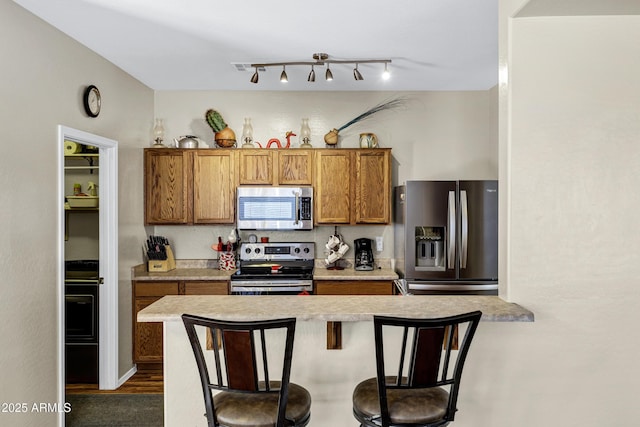 110 E Saddle Way, San Tan Valley, AZ 85143 - kitchen with appliances with stainless steel finishes, brown cabinetry, a breakfast bar, light countertops, and dark wood-style flooring