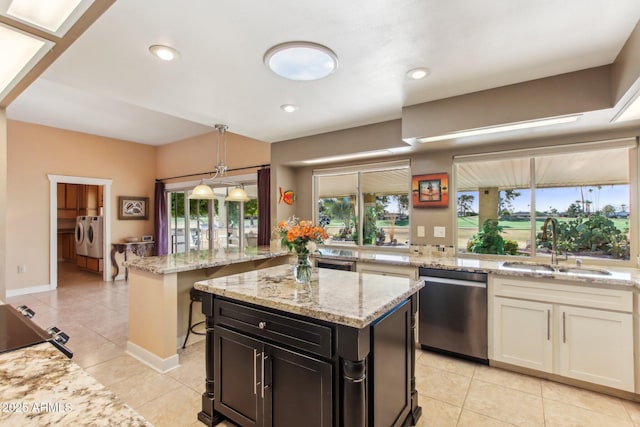 kitchen featuring light stone countertops, sink, separate washer and dryer, stainless steel dishwasher, and a kitchen island