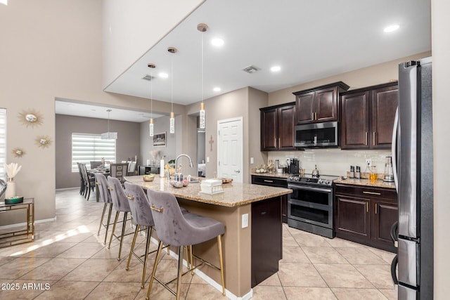 kitchen featuring a breakfast bar area, a center island with sink, visible vents, light tile patterned flooring, and stainless steel appliances