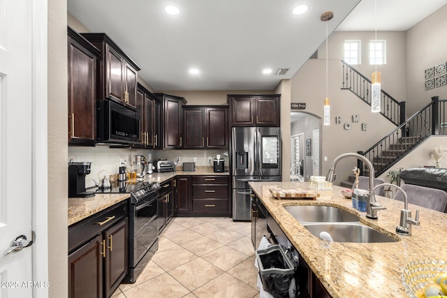 kitchen with a sink, light stone countertops, dark brown cabinetry, and black appliances