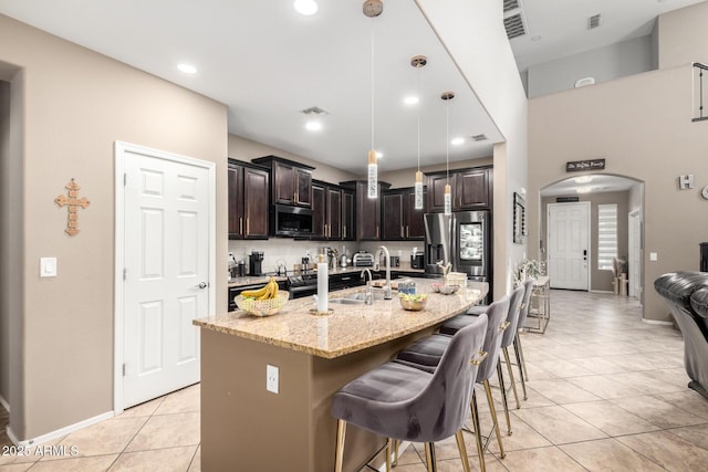 kitchen featuring a breakfast bar, a sink, arched walkways, appliances with stainless steel finishes, and light tile patterned floors