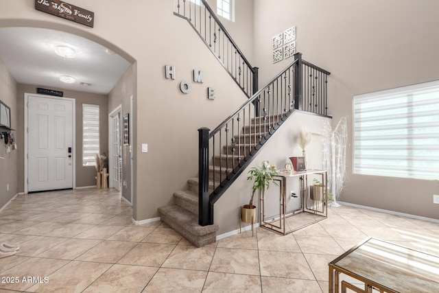 tiled entrance foyer with arched walkways, stairway, baseboards, and a towering ceiling