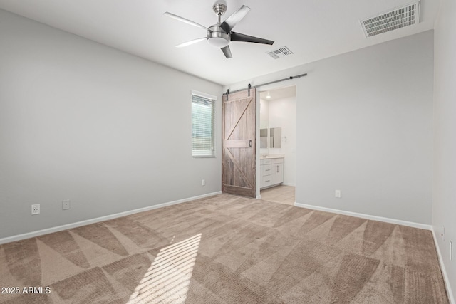 unfurnished bedroom featuring light carpet, a barn door, ceiling fan, and ensuite bathroom