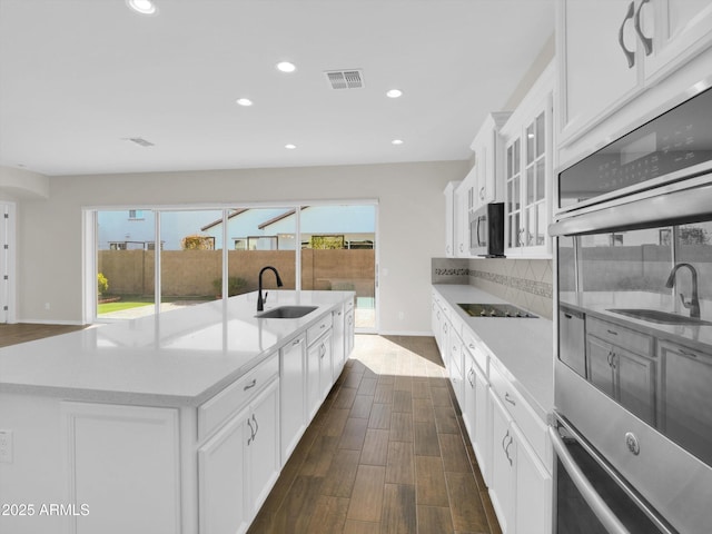 kitchen featuring sink, white cabinetry, stainless steel appliances, a center island with sink, and decorative backsplash