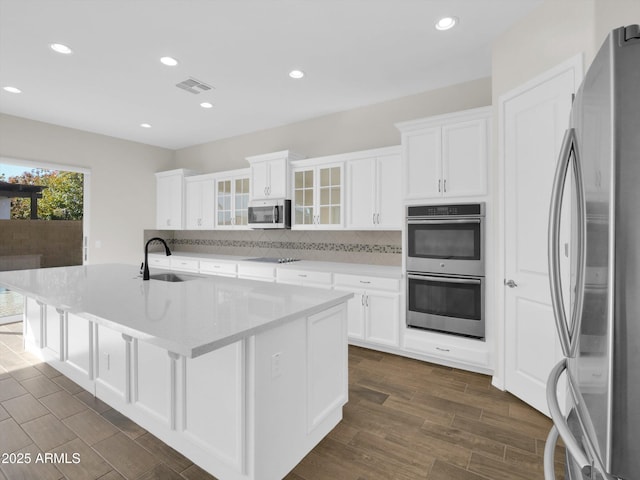 kitchen featuring sink, white cabinetry, a center island with sink, appliances with stainless steel finishes, and decorative backsplash