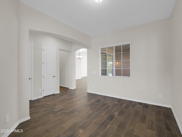 unfurnished room with a notable chandelier and dark wood-type flooring