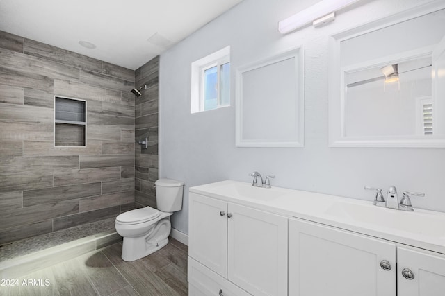 bathroom with a tile shower, vanity, and toilet