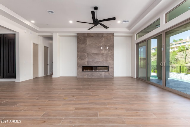 unfurnished living room featuring a raised ceiling, ceiling fan, light wood-type flooring, and a premium fireplace