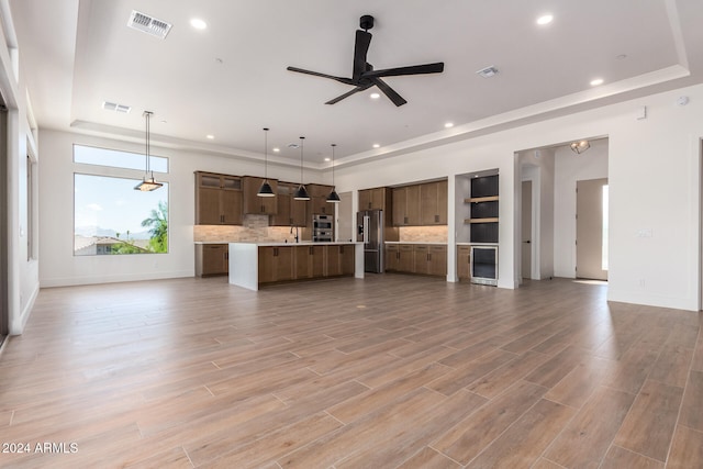 unfurnished living room with ceiling fan, light wood-type flooring, and a tray ceiling