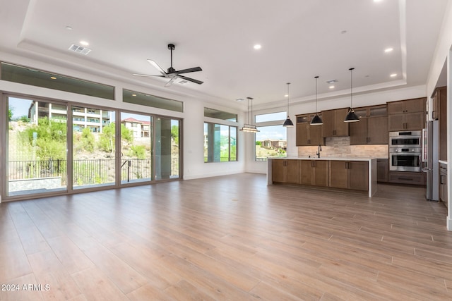 unfurnished living room featuring a raised ceiling, ceiling fan, and light hardwood / wood-style flooring