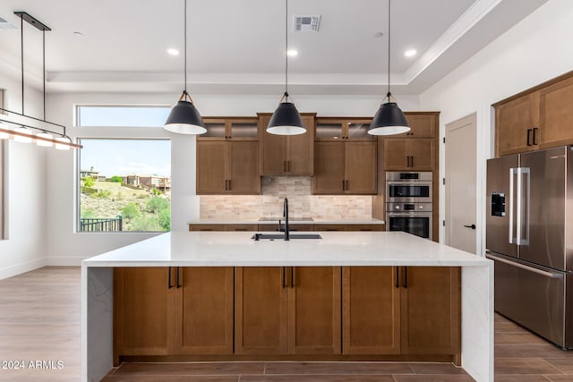 kitchen with sink, stainless steel appliances, hanging light fixtures, and an island with sink