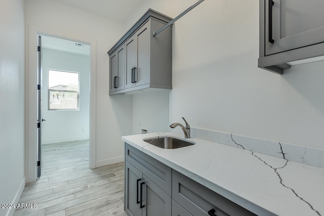 kitchen with gray cabinetry, light stone countertops, sink, and light hardwood / wood-style flooring