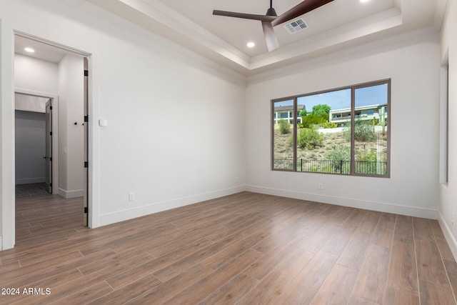 unfurnished room with hardwood / wood-style floors, ceiling fan, a raised ceiling, and crown molding