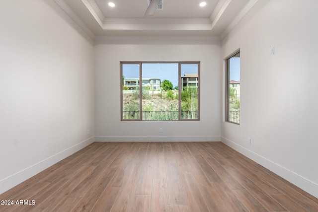 empty room featuring wood-type flooring, a raised ceiling, and ornamental molding