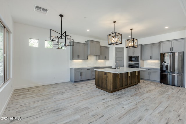 kitchen with stainless steel refrigerator with ice dispenser, light wood-type flooring, hanging light fixtures, and an island with sink