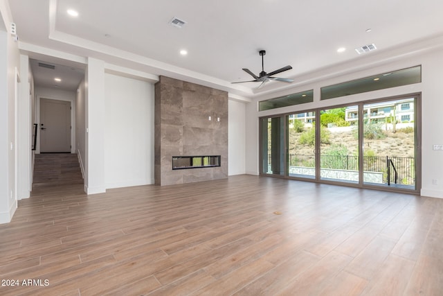 unfurnished living room featuring a tile fireplace, light hardwood / wood-style floors, and ceiling fan