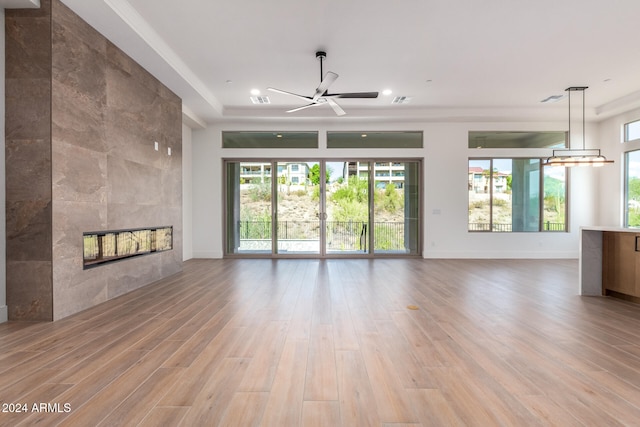 unfurnished living room featuring a tile fireplace, light hardwood / wood-style flooring, ceiling fan, and a healthy amount of sunlight