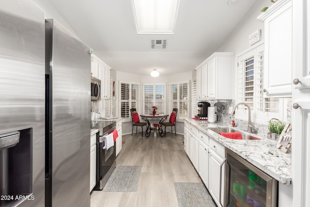 kitchen with beverage cooler, white cabinets, light hardwood / wood-style flooring, sink, and appliances with stainless steel finishes