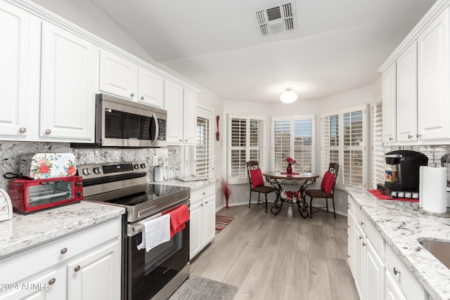 kitchen with white cabinets, light hardwood / wood-style floors, appliances with stainless steel finishes, and tasteful backsplash