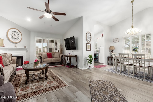 living room with high vaulted ceiling, beverage cooler, light hardwood / wood-style floors, and ceiling fan with notable chandelier