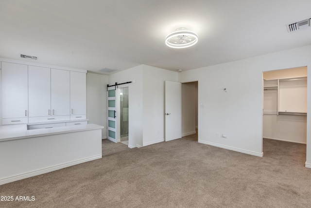 unfurnished bedroom featuring carpet floors, a barn door, visible vents, and a walk in closet