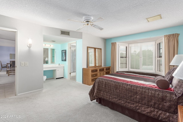 bedroom featuring a textured ceiling, light colored carpet, ensuite bath, and ceiling fan