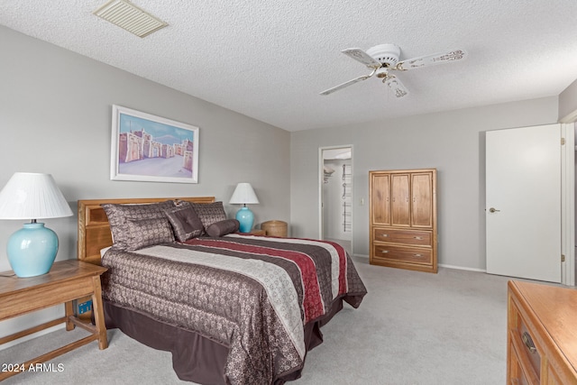 carpeted bedroom featuring a walk in closet, a textured ceiling, a closet, and ceiling fan