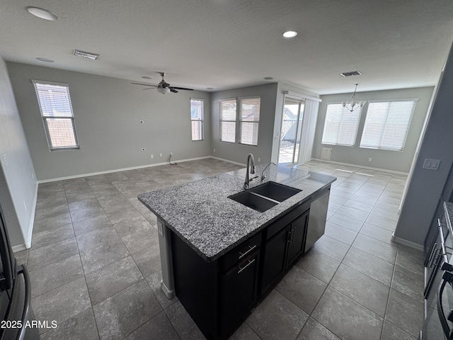 kitchen featuring sink, a center island with sink, a textured ceiling, and light stone counters