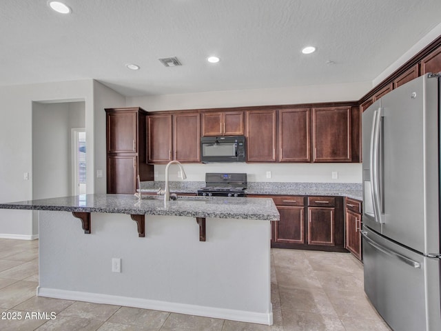 kitchen featuring sink, an island with sink, a kitchen bar, stainless steel fridge with ice dispenser, and gas range