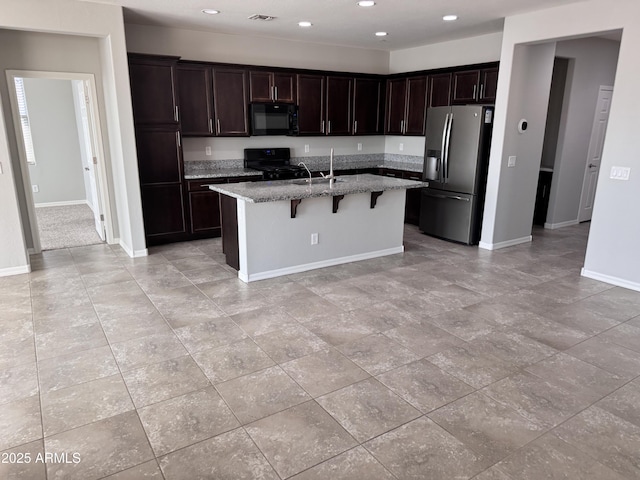 kitchen with a breakfast bar, sink, light stone countertops, a kitchen island with sink, and black appliances