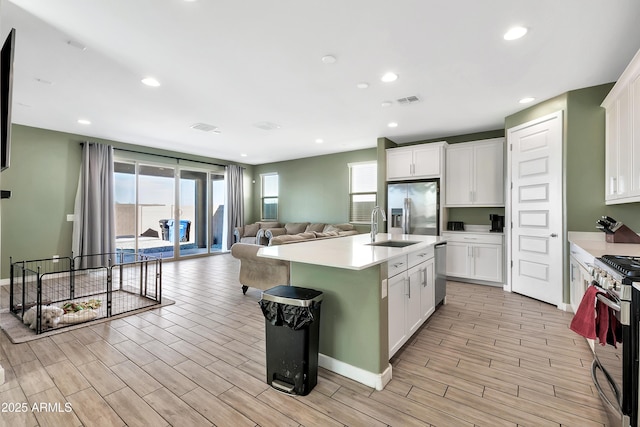 kitchen with an island with sink, appliances with stainless steel finishes, sink, and white cabinets