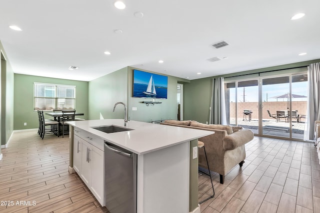 kitchen with sink, dishwasher, white cabinetry, a kitchen breakfast bar, and an island with sink