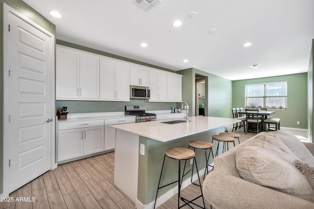 kitchen with sink, appliances with stainless steel finishes, a kitchen breakfast bar, an island with sink, and white cabinets