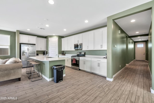 kitchen with appliances with stainless steel finishes, a center island with sink, and white cabinets