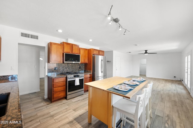 kitchen with stainless steel appliances, light hardwood / wood-style flooring, tasteful backsplash, light stone counters, and a breakfast bar area