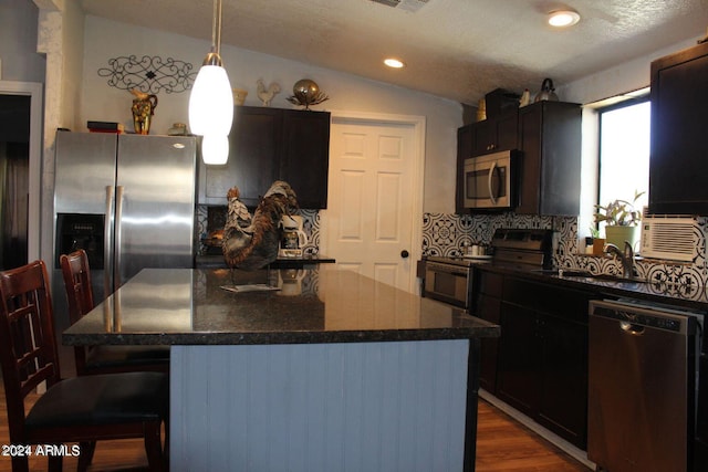 kitchen featuring hanging light fixtures, a center island, dark wood-type flooring, stainless steel appliances, and a kitchen breakfast bar