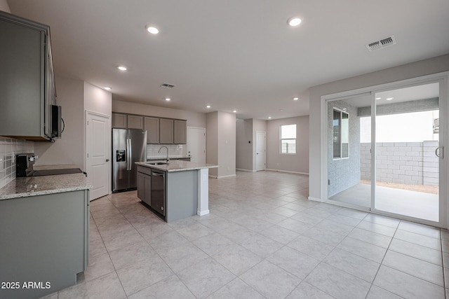 kitchen featuring backsplash, light stone counters, stainless steel appliances, sink, and an island with sink