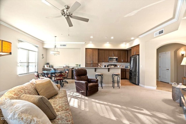 living room with ceiling fan, ornamental molding, and light carpet