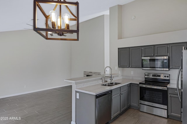 kitchen with an inviting chandelier, a peninsula, gray cabinets, a sink, and stainless steel appliances