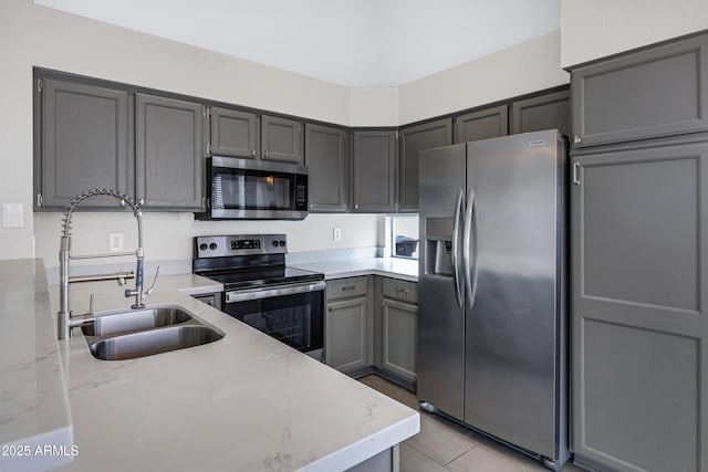 kitchen featuring light tile patterned floors, a sink, appliances with stainless steel finishes, gray cabinetry, and light stone countertops