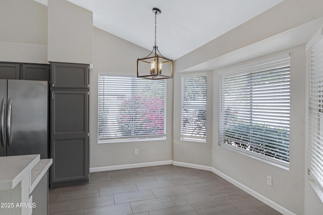 unfurnished dining area with a notable chandelier, baseboards, and vaulted ceiling