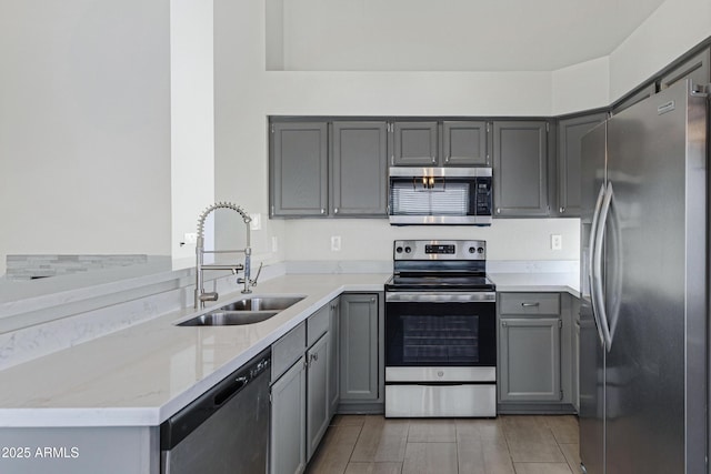 kitchen with stainless steel appliances, gray cabinetry, a sink, and light stone counters