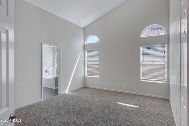 carpeted empty room with high vaulted ceiling and baseboards