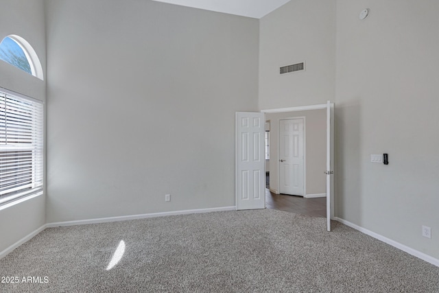 carpeted spare room with visible vents, baseboards, a high ceiling, and a healthy amount of sunlight
