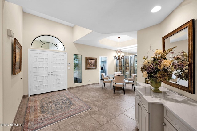 foyer featuring stone finish floor, baseboards, a notable chandelier, a tray ceiling, and recessed lighting