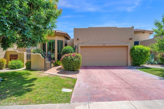 pueblo-style house featuring an attached garage, a tile roof, a front lawn, stucco siding, and driveway