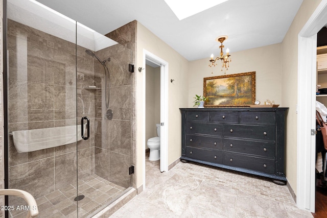 bathroom featuring a skylight, a stall shower, a chandelier, and toilet