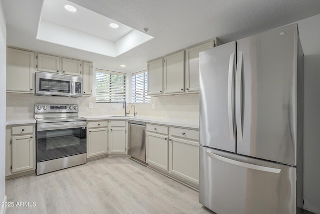 kitchen featuring sink, light wood-type flooring, stainless steel appliances, and a raised ceiling